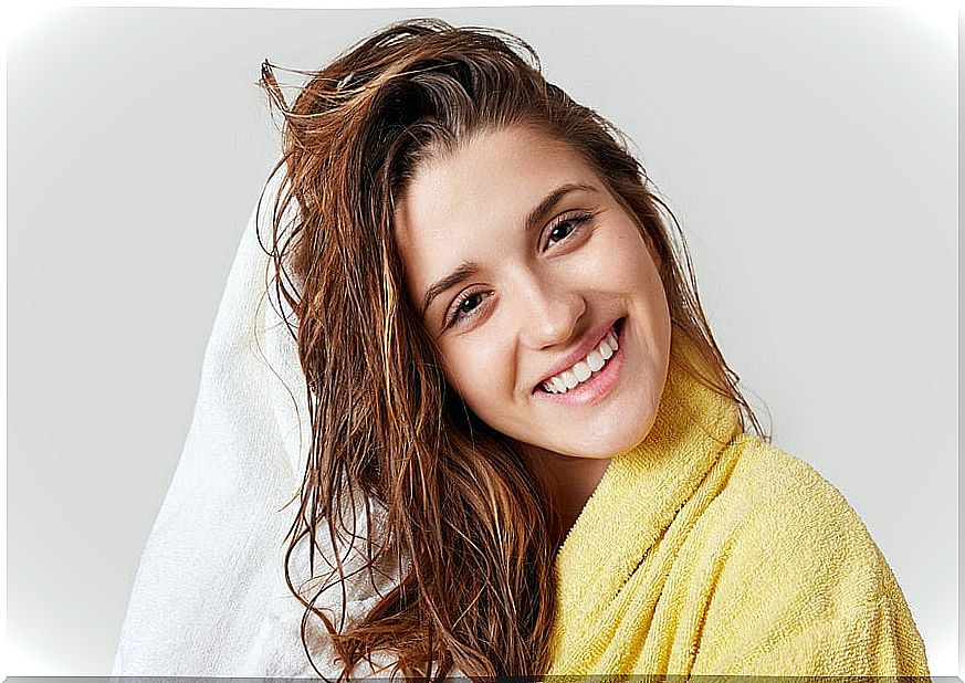 Smiling woman dries her hair with a white towel.